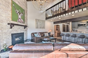 Amplia sala de estar con chimenea, un sofá, una mesa de centro y una zona de cocina con taburetes de bar.