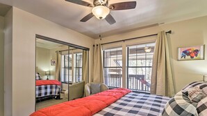 Une chambre à coucher avec un lit, un ventilateur de plafond, une fenêtre avec des rideaux et un tableau au mur.