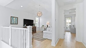 Een ruime woonkamer met een witte balustrade, een grote televisie en een kroonluchter.