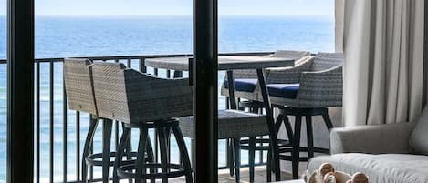 A balcony with a view of the ocean, a dining area with chairs and tables, and a sofa.