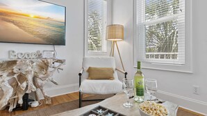 A room with a television, a white chair, a lamp, a table with snacks and drinks, and a decorative piece. - Ocean Views + Walk to Beach + Golf Cart Included! (Santa Rosa Beach)