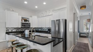 A modern kitchen with white cabinets, a black countertop, stainless steel appliances, and a bar stool area. - Gulf Views | Rooftop Patio | Heated Pool (Santa Rosa Beach)
