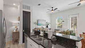 A modern kitchen with a black granite countertop, stainless steel sink, and white cabinetry. There is a dining area with a green sofa and a wooden table. - Gulf Views | Rooftop Patio | Heated Pool (Santa Rosa Beach)