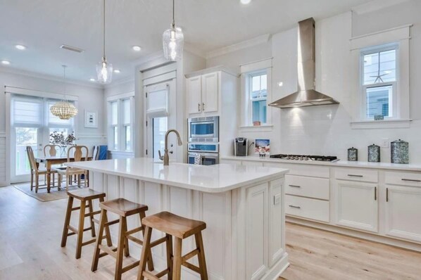 A spacious kitchen with white cabinetry, a large island with stools, and a stainless steel range hood.