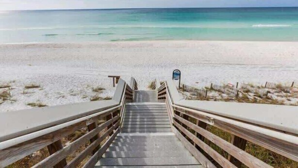 Un escalier en bois menant à une plage d’où l’on a une vue dégagée sur l’océan.