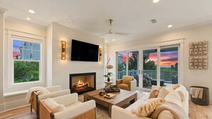 A modern living room with a fireplace, comfortable seating, and large windows offering a view of the outdoors. - Gulf View Estate | Private Pool | Walk to Beach (Inlet Beach)