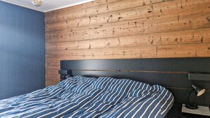 A bedroom with a wooden headboard, a striped bedspread, and a bedside lamp.