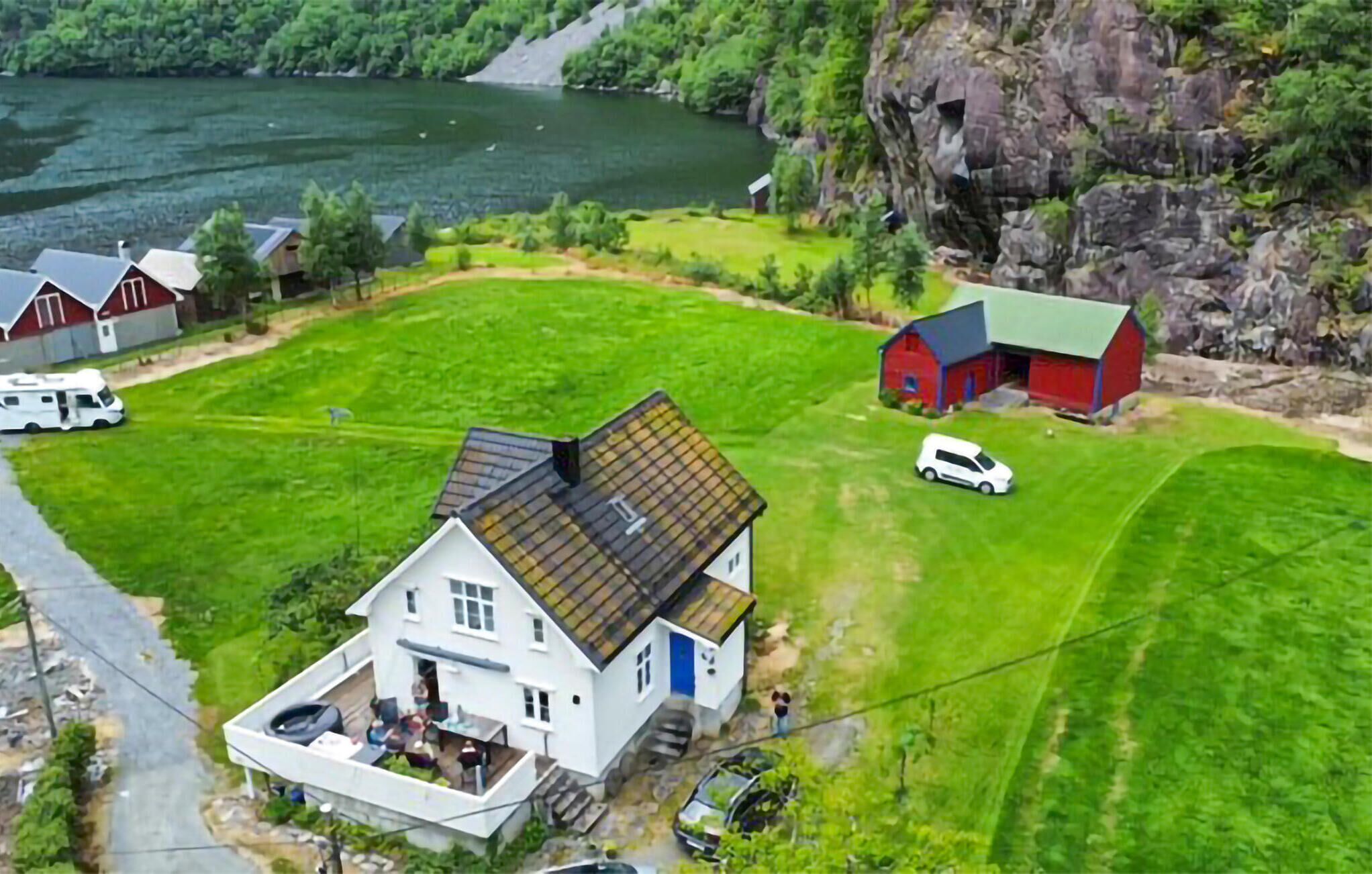 A rural house with a porch, a barn, and a white van in a green field near a lake.