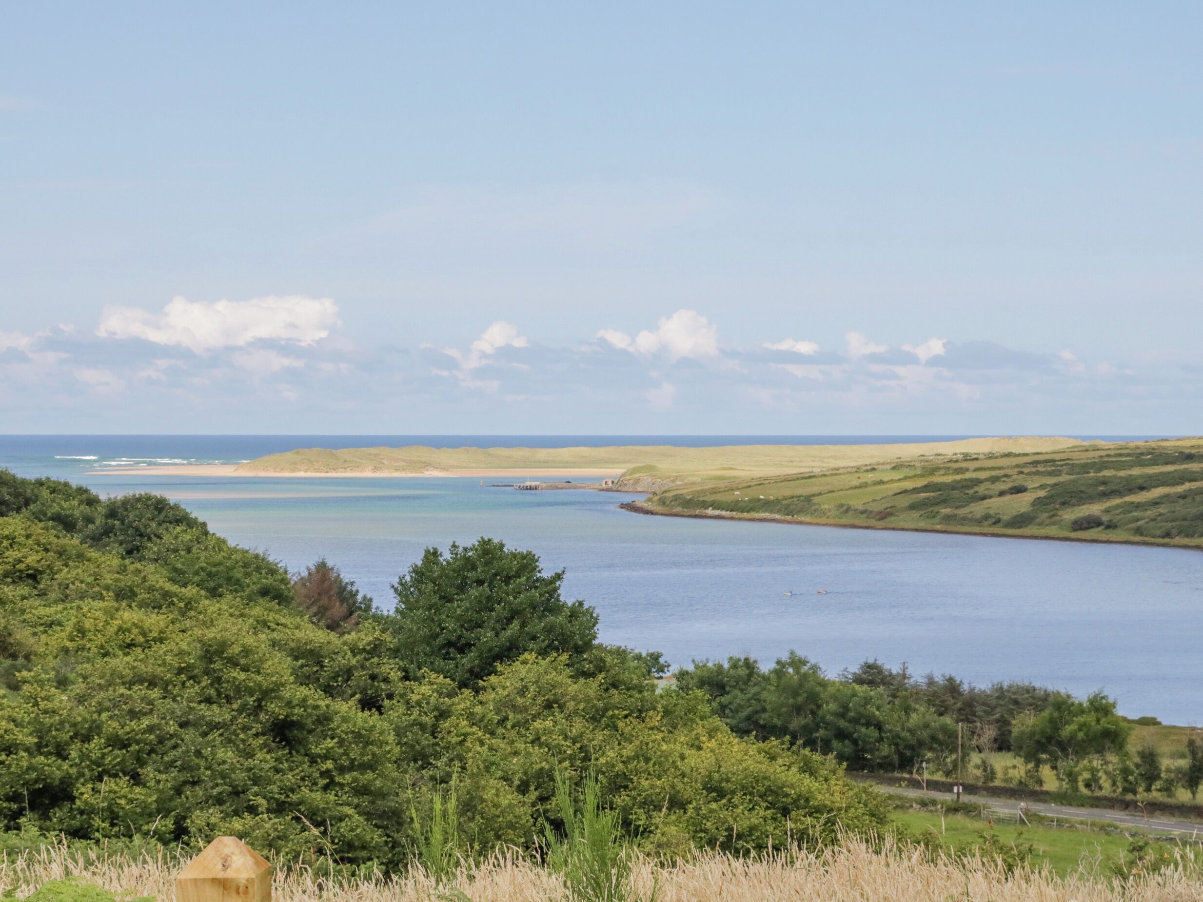 A coastal landscape with a clear view of the sea, rolling hills, and dense greenery.