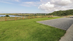 Zona verde con cerca de madera, un camino de grava y vista a un lago y colinas a lo lejos.