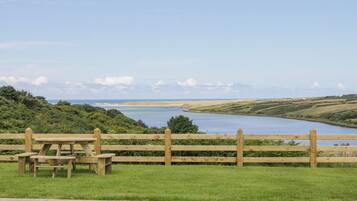 A picnic area with a wooden fence and benches overlooking a body of water and distant landscape.