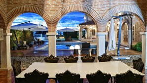 Un espace extérieur aménagé avec une terrasse, une piscine, des coins salon couverts et une table à manger avec des chaises.
