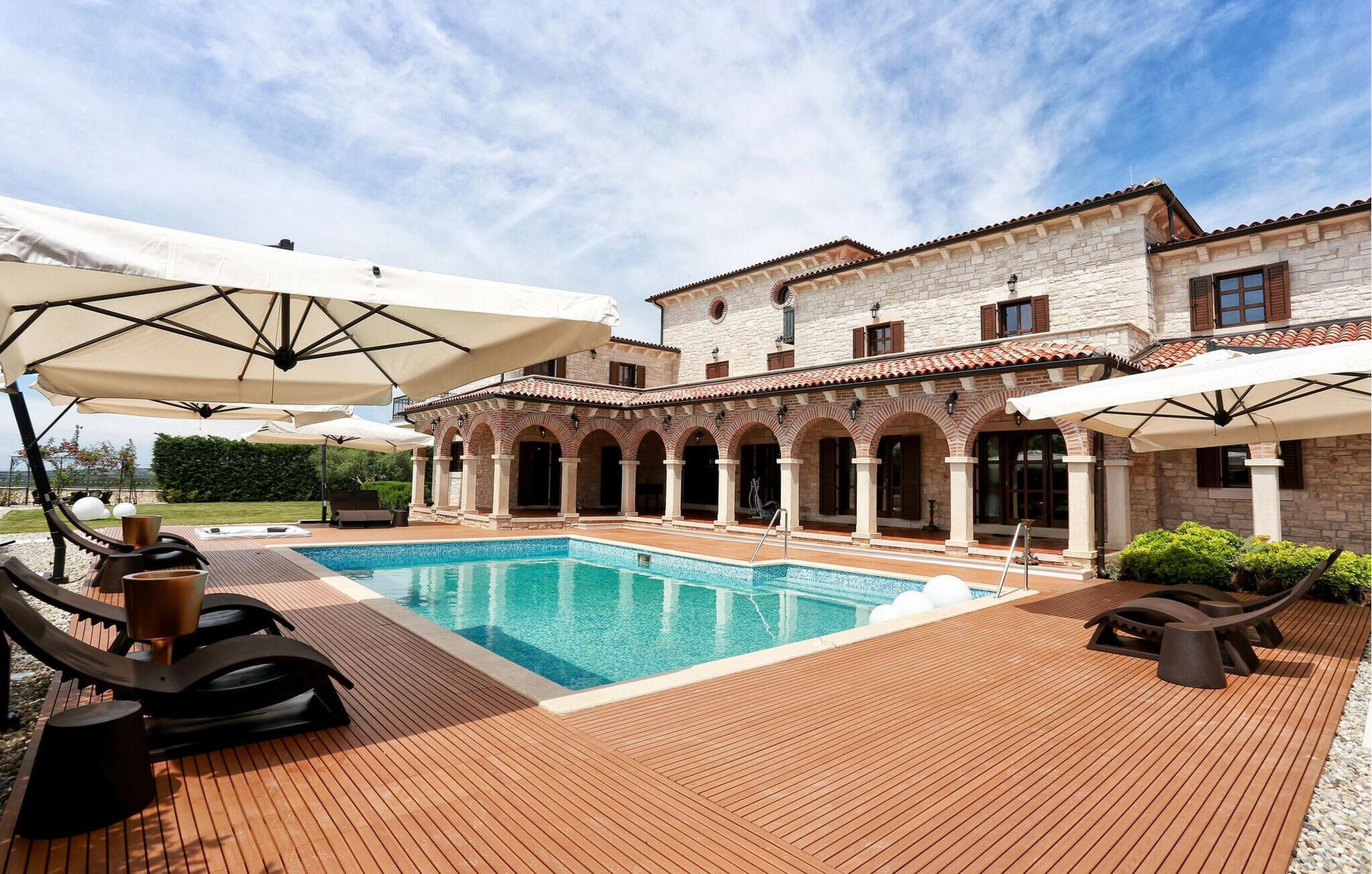 A pool area with a stone building, outdoor seating, and umbrellas.