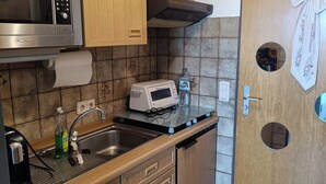 A compact kitchen with a microwave, toaster, sink, and wooden cabinets. - Ferienwohnung Sielluft (Dornum)