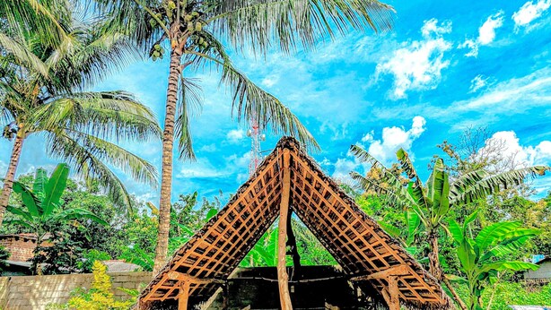 A rustic hut with a triangular roof structure, surrounded by lush greenery and palm trees. - Maika safari (Udawalawa)