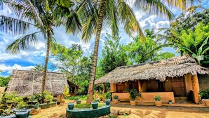 A rustic village with thatched-roof huts surrounded by lush greenery and palm trees. - Maika safari (Udawalawa)