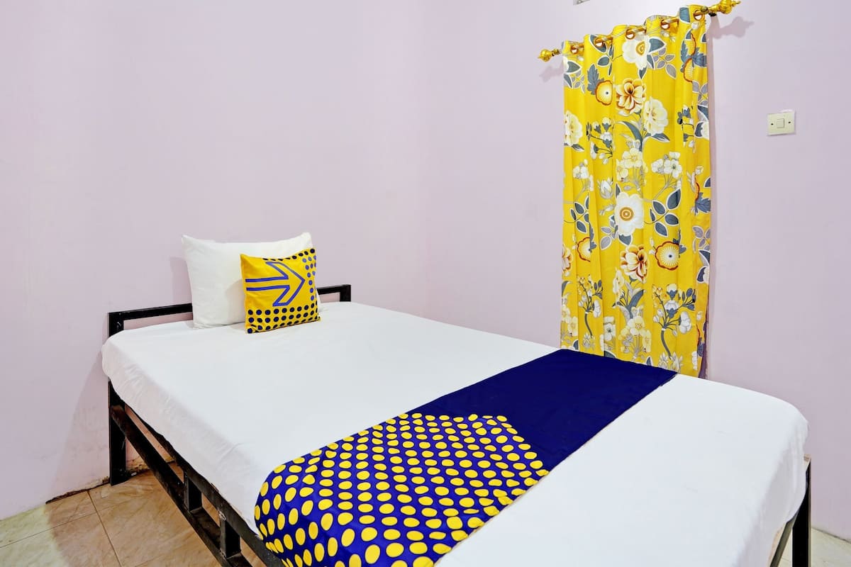 Una cama individual con colchón blanco, colcha de diseño azul y amarillo, y almohada blanca con diseño geométrico.