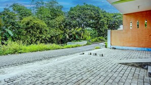 A paved pathway leading to a building with a green and orange facade, surrounded by lush greenery. - Hotel O Kemangi Asri Kost (Banyuwangi)