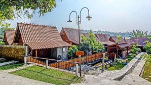 A row of traditional wooden houses with tiled roofs, a small bridge, and a clear view of the surrounding landscape. - Collection O 91582 Green Kasongan Cottage (Kasihan)