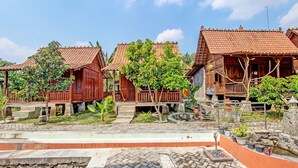 A traditional wooden house with a tiled roof, surrounded by a garden with a small pond and potted plants. - Collection O 91582 Green Kasongan Cottage (Kasihan)