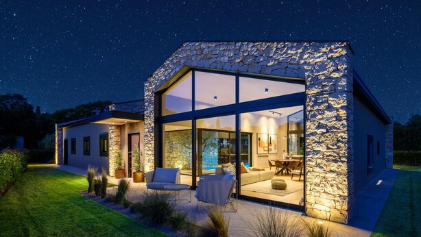 A modern house with large glass windows, a stone exterior, and a well-lit outdoor seating area. - Stunning home in Bale (Bale)