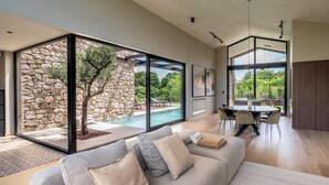 A modern living room with a large glass wall, a stone wall, and a pool view. - Stunning home in Bale (Bale)
