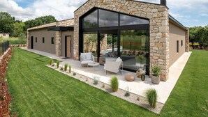 A modern house with a stone facade, large glass windows, and a patio with outdoor furniture. - Stunning home in Bale (Bale)