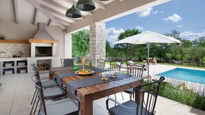 Eine Außenpatio mit einem langen Holztisch, Stühlen, einem Grill und einem Pool im Hintergrund.