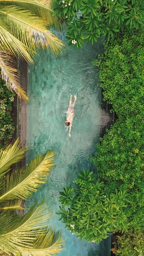 Una persona nadando en una piscina cristalina rodeada de abundante vegetación.