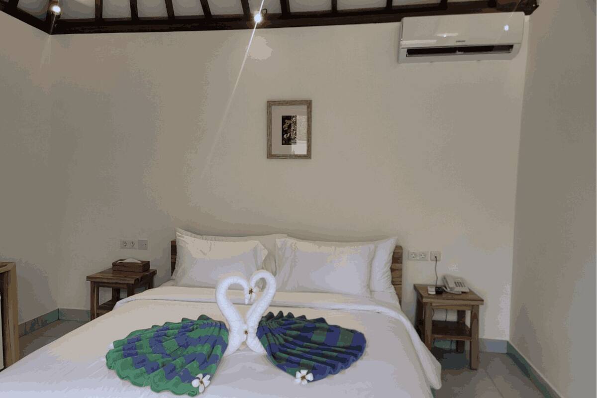 A hotel room with a bed, two nightstands, an air conditioning unit, and a framed picture on the wall.
