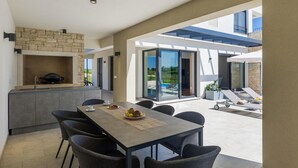 Eine moderne Küche mit Steinrückwand, ein Essbereich mit Tisch und Stühlen sowie Blick auf einen Pool und eine Außenlounge.
