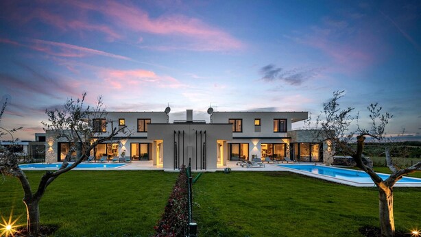 Ein modernes, zweistöckiges Haus mit Swimmingpool, umgeben von einem gepflegten Rasen und Bäumen.