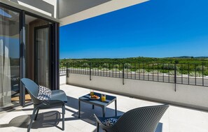 Enjoy a serene view of the lush landscape from this balcony, featuring a table for dining and comfortable seating.