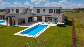 Ein modernes, zweistöckiges Haus mit großem Swimmingpool, Sitzgelegenheiten im Freien und einem Whirlpool.