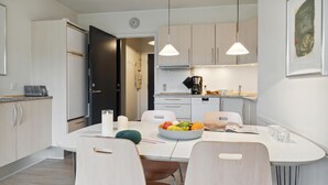 Moderni keittiö, jossa on valkoiset kaapit, ruokapöytä tuoleineen, hedelmäkulho ja riippuvalaisimet.