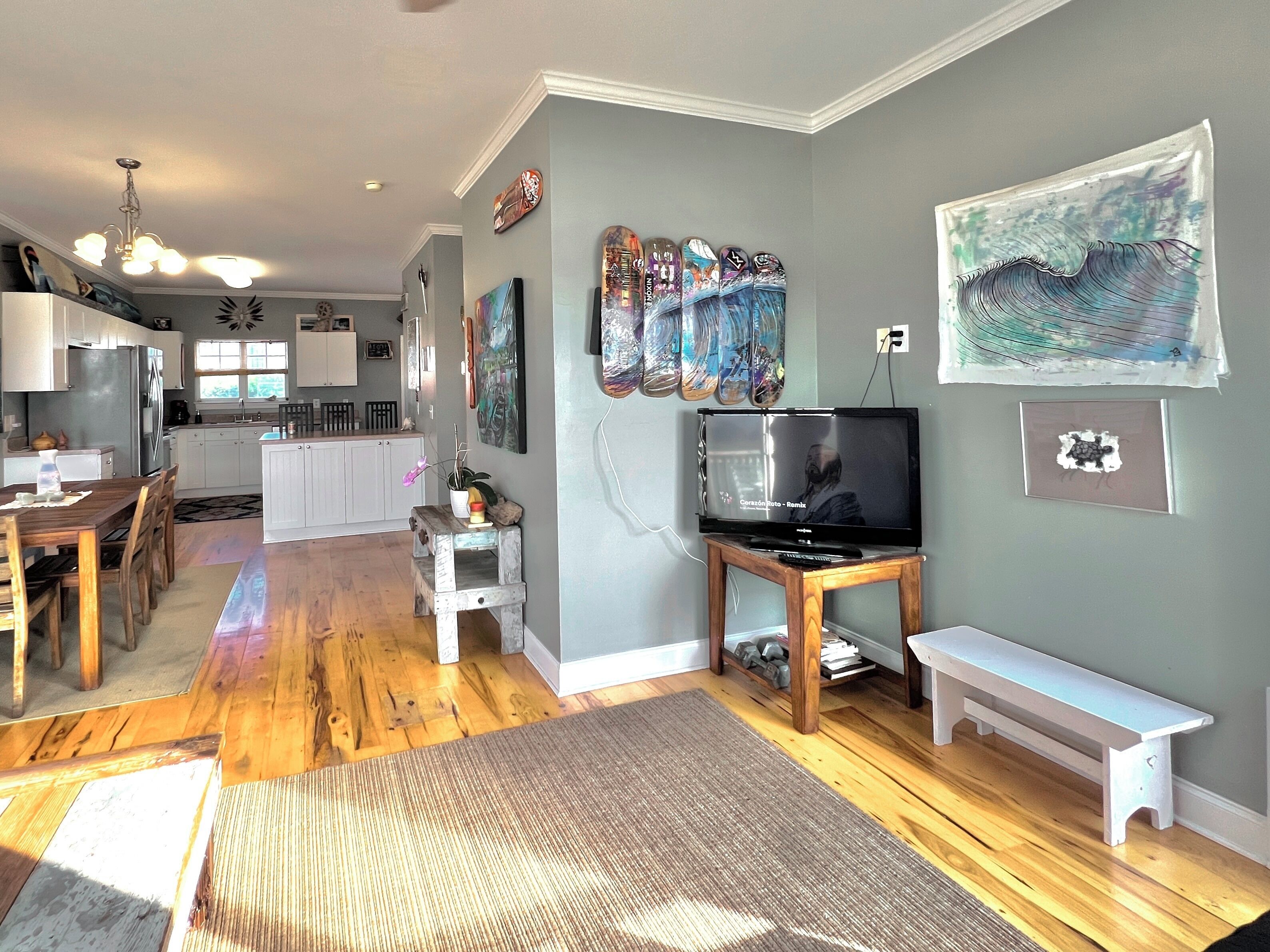 A modern living room with a wooden floor, a dining area with a table and chairs, a kitchen with white cabinets, and a TV on a stand.