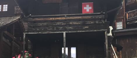 Una cabaña de madera tradicional con balcón, una bandera suiza y un arreglo floral.