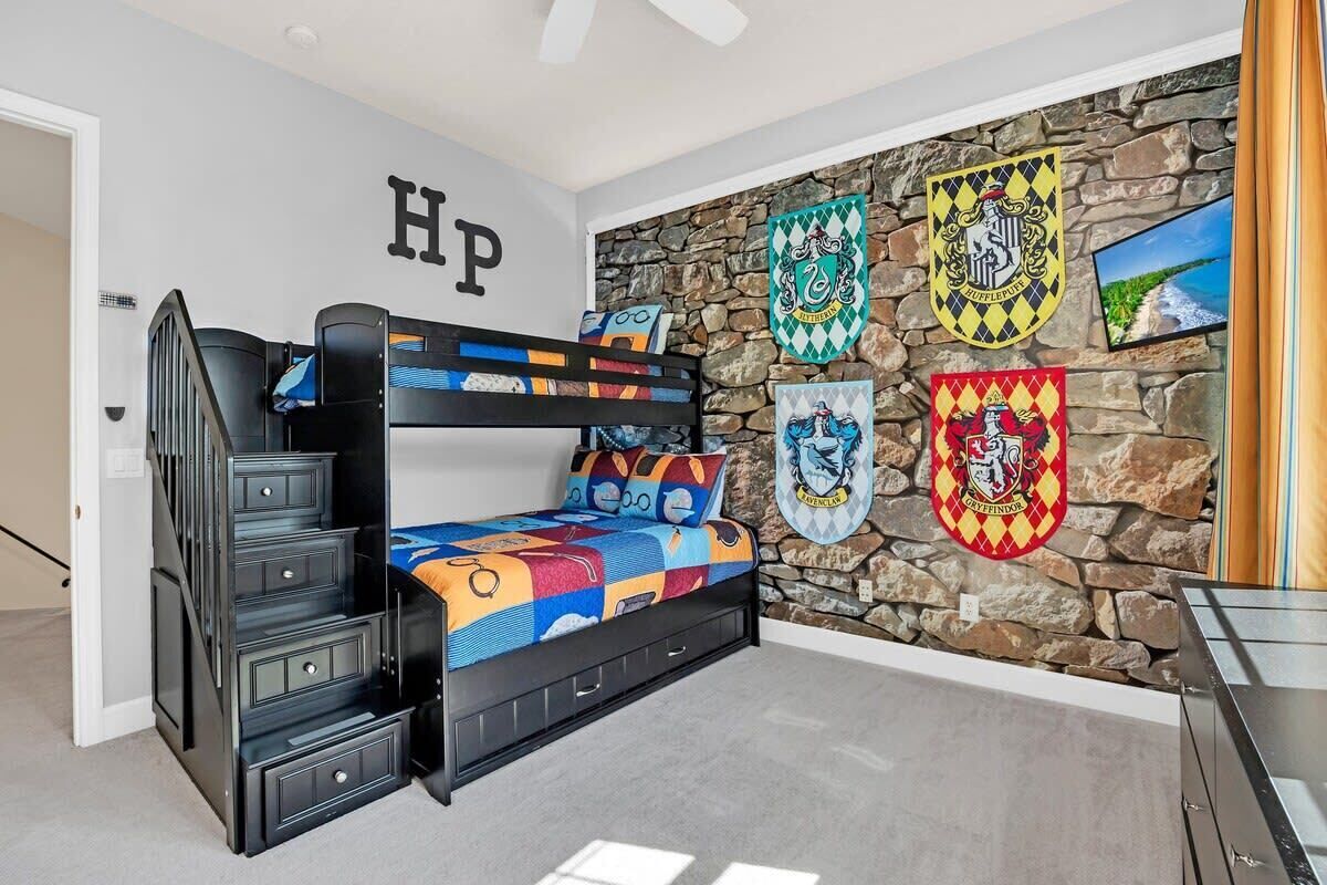 A bunk bed with a colorful quilt, a stone wall with crest decorations, and a "HP" sign on the wall.