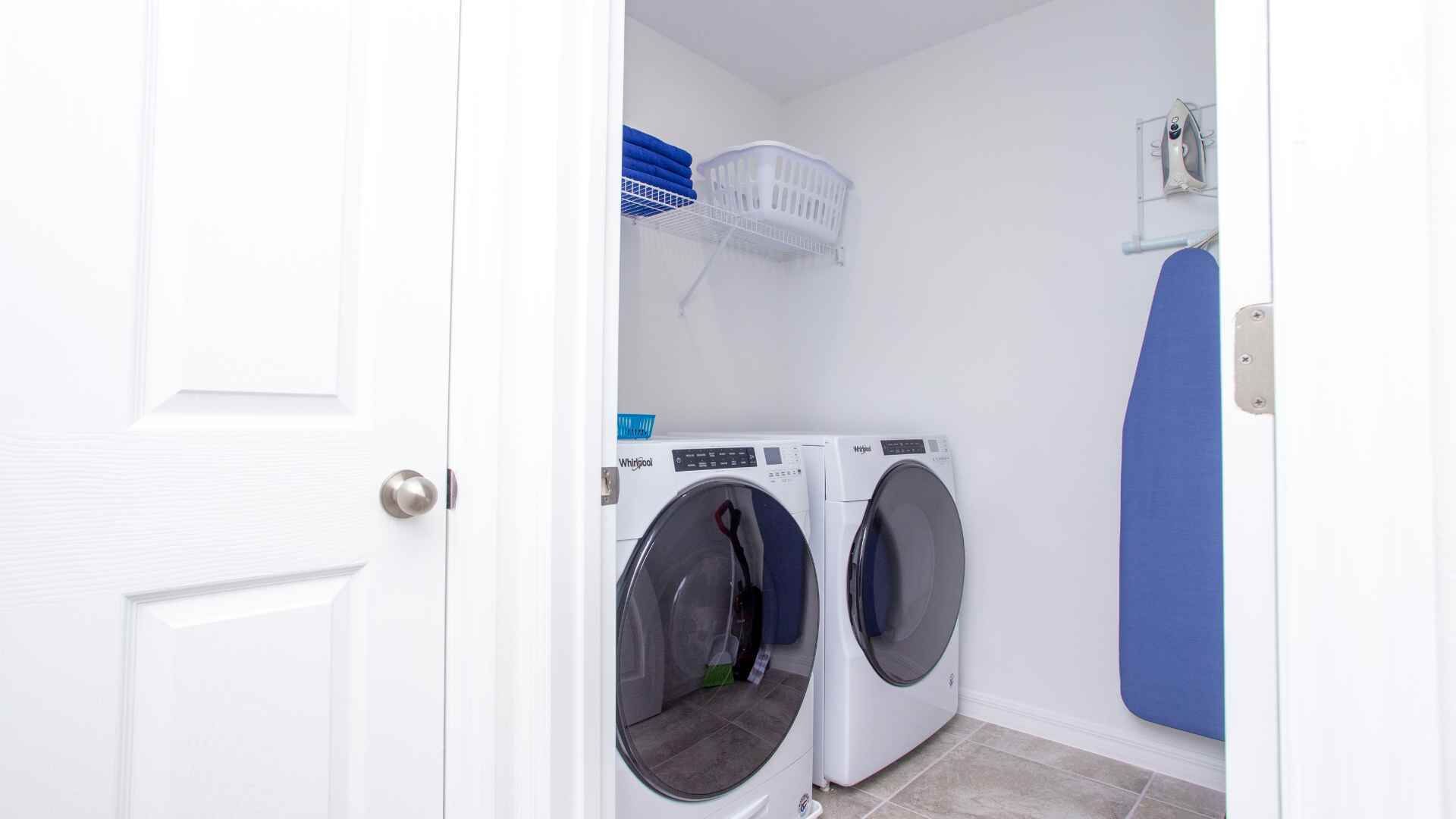 Een wasserette met twee voorladers, een blauwe droogrek en een witte mand aan de muur.