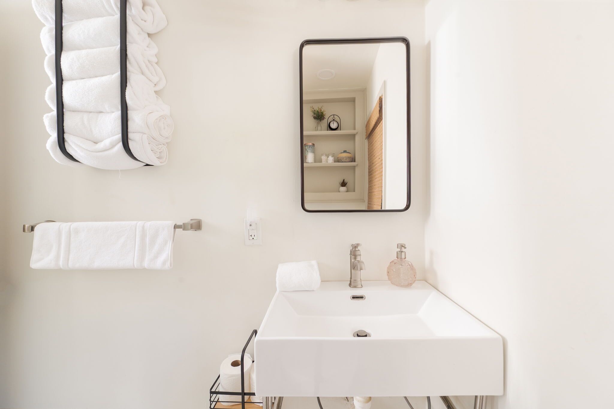 Un baño moderno con un lavabo blanco, un espejo y un perchero para toallas.