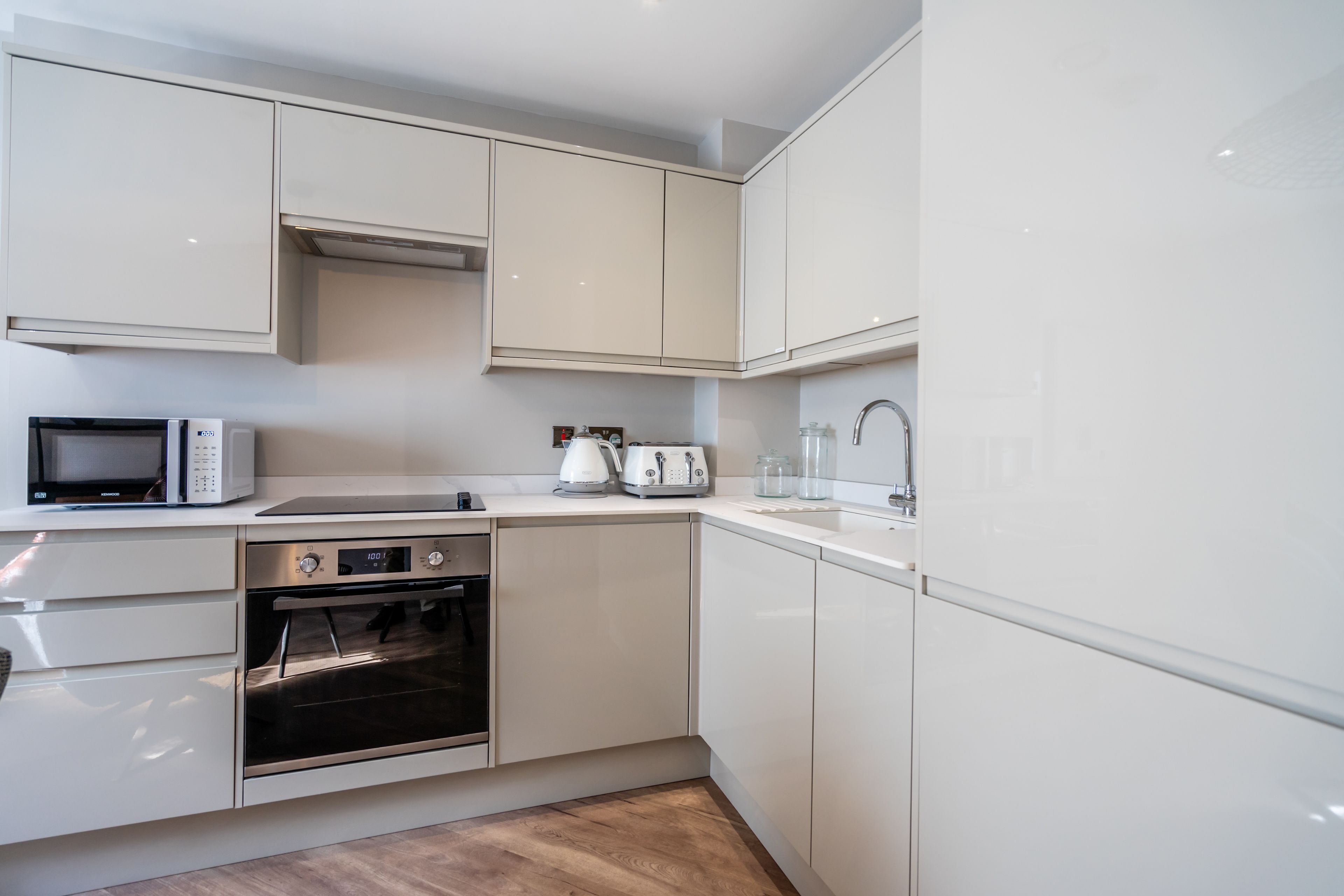 A modern kitchen with white cabinetry, a microwave, an oven, a kettle, and a toaster.