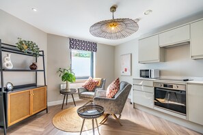 A modern kitchen with a built-in oven and microwave, a dining area with a round rug, and a seating area with a chair and cushions. - A couples retreat that sleeps 2 guests in 1 bedroom (York)