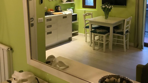 A room with a green wall, a wooden ceiling, a chandelier, a dining table with chairs, a kitchen area with cabinets and a stove, and a television mounted on the wall. - 1BR Apt in Via Panicale by Sea N' Rent (Florence)