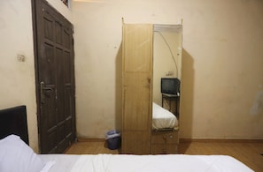 Una habitación pequeña con cama, armario de madera, espejo y televisor.