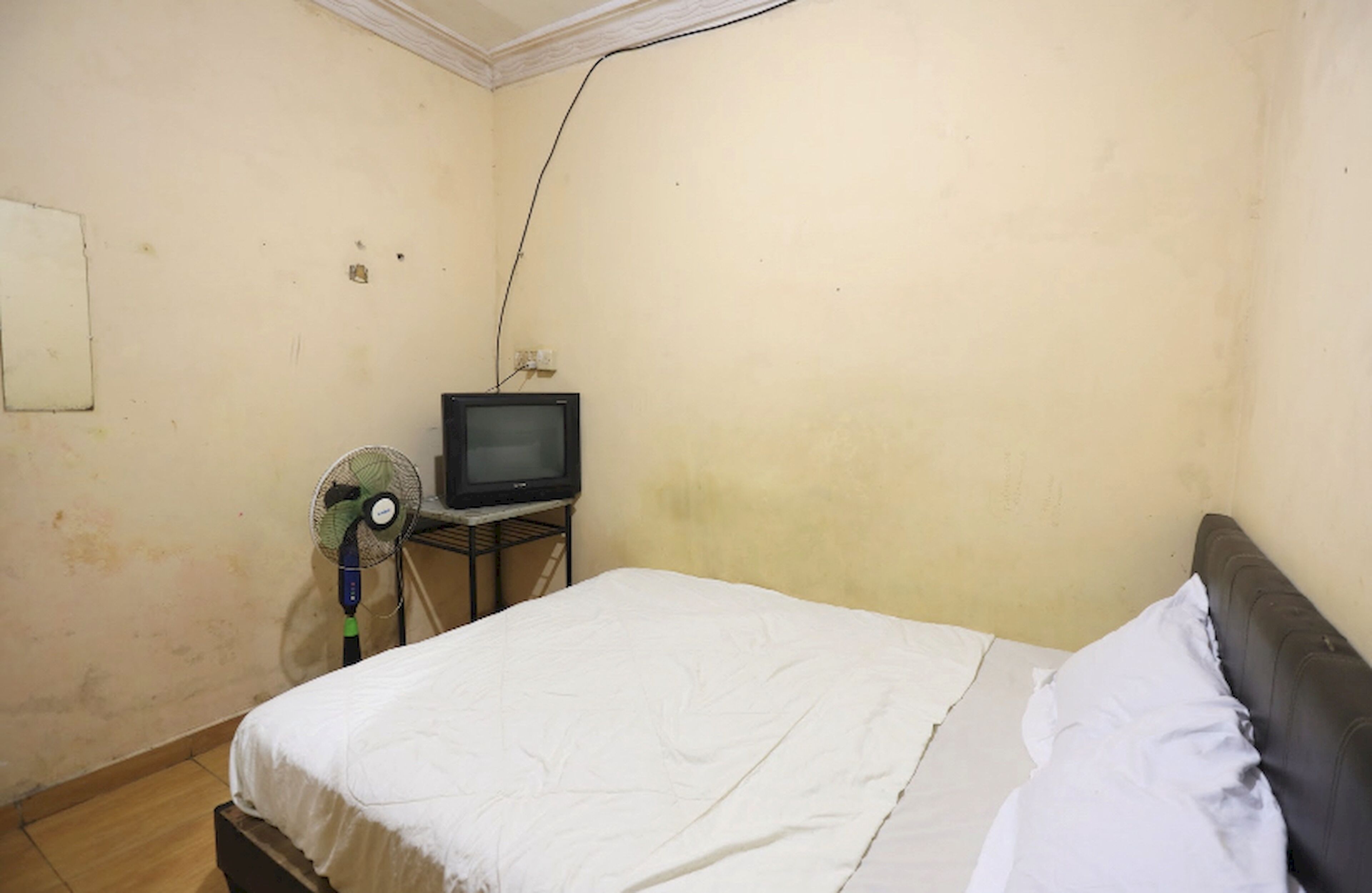Une petite pièce simple, avec un lit, une télévision et un ventilateur.