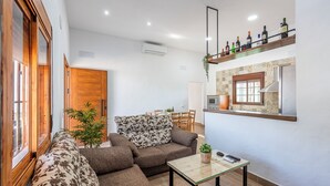 A modern living room with a sofa, a coffee table, and a kitchen area with a shelf of bottles. - Holiday Home Adalid, Seville Countryside (La Puebla de Cazalla)