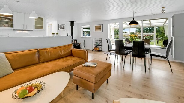 Una sala de estar moderna con un sofá, un comedor con sillas y una mesa, y una cocina con armarios blancos.