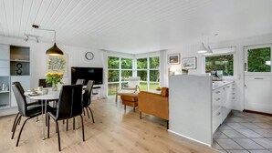 Una cocina moderna con armarios blancos, un comedor con mesa y sillas redondas, y una sala de estar con sofá y mesa de centro.