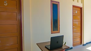 A hallway with doors numbered 4 and 5, a laptop on a table, and a potted plant. - Hotel O Putri Guest House Syariah Near SPBU Rimbo Panjang (Pekanbaru)