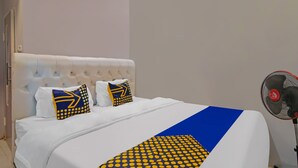 A neatly made bed with white bedding, two pillows with yellow and blue patterns, and a blue and yellow blanket. A standing fan is visible to the right. - Hotel O Putri Guest House Syariah Near SPBU Rimbo Panjang (Pekanbaru)